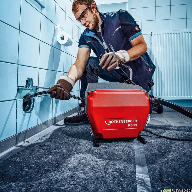 Rohrreiniger mit Bediener schiebt die Spirale in einen verstopften Toilettenrohr im Bad.