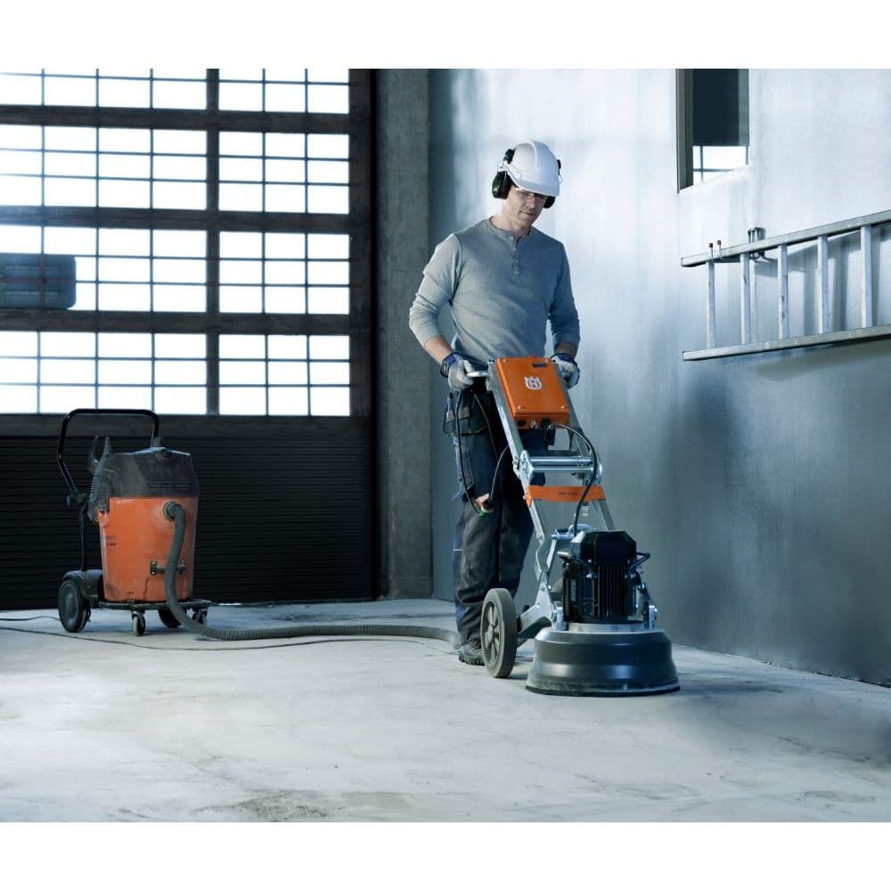 Der Bodenschleifer mit Bediener und angeschlossenen Industriesauger beim Schleifen eines Betonbodens